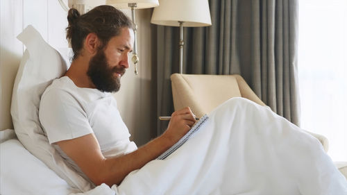 Man holding book while sitting on bed at home