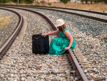 Full length of woman with luggage sitting on railroad track