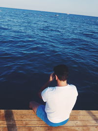 Rear view of man sitting on sea against sky