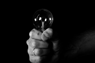 Cropped hand holding light bulb against black background