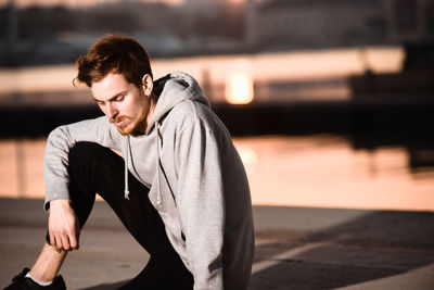 Young man looking away while standing against sky during sunset