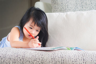 Girl writing in book on sofa at home