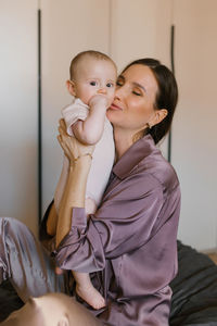 Mother lifts the baby up in her arms, kissing him on the cheek