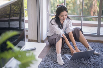 Young woman using phone while sitting on window