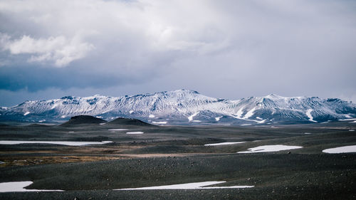 Scenic view of landscape and snowcapped mountains against cloudy sky