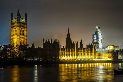 Illuminated buildings by river against sky in city at night