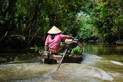 Rear view of woman in boat on river against trees