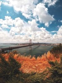 Suspension bridge over river against cloudy sky