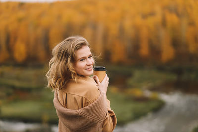 A pretty girl enjoys solitude drinks coffee walks in the autumn forest in nature in fall