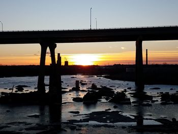 Silhouette bridge over river against sky during sunset