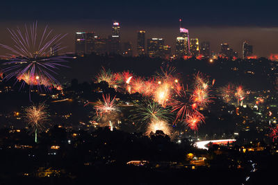 Firework display in city against sky at night