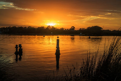 Silhouette of wooden posts in lake against sky during sunset