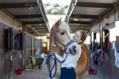 Woman caring for horse standing in stable