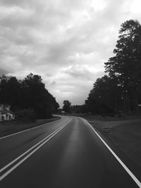 Road amidst trees against cloudy sky