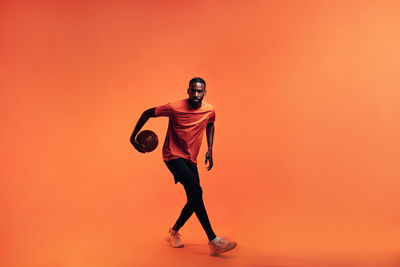 Full length of young man standing against orange background