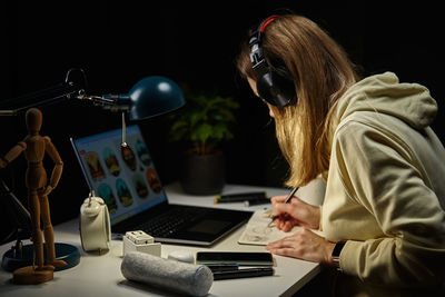 Woman working from home workplace at night, using laptop