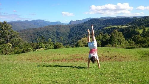 Woman doing handstand on grass against sky