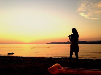 Rear view of silhouette woman standing at beach against sky during sunrise