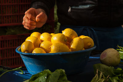 Midsection of man with lemons in container at market