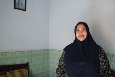 Portrait of smiling young woman standing against wall