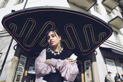 Low angle portrait of young woman standing at entrance of building in city