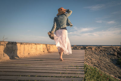 Full length of woman walking on boardwalk against sky