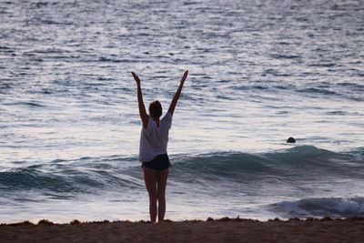 Rear view of woman with arms raised standing on shore at beach