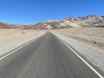 Road leading towards mountains against clear blue sky