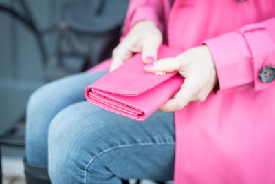 Midsection of woman holding pink purse while sitting outdoors