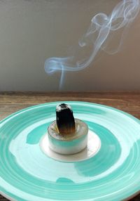 Incense burning in blue plate on table