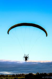 Man powered paragliding against blue sky