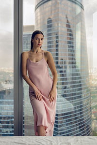 Woman in a nightgown stands at the window in a skyscraper near the bed