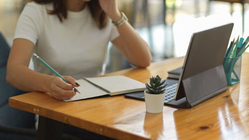 Midsection of woman using mobile phone while sitting on table