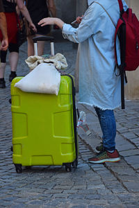 Low section of woman standing with luggage on footpath