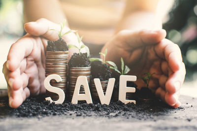 Cropped image of hands with seedlings on stacked coins and text