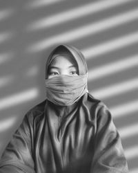 Portrait of girl wearing hijab and mask against wall