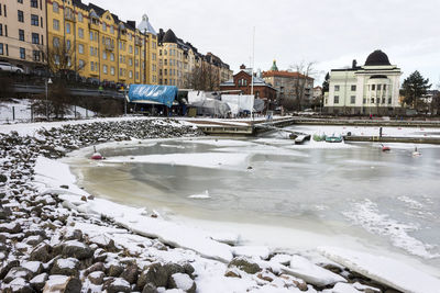 Frozen river by buildings in city