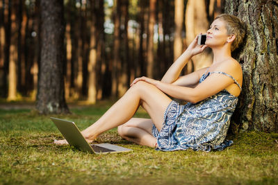 Woman talking on phone while using laptop in forest