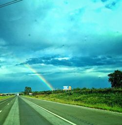 Rainbow over agricultural field against cloudy sky