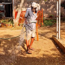 Full length of senior man holding garden hose on field 