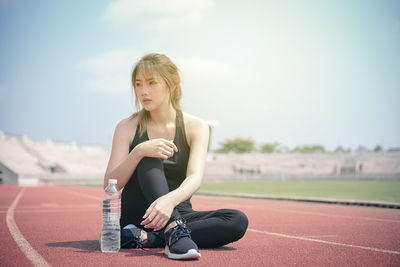 Young woman looking away while sitting on running track