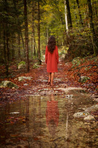 Woman in red dress walking barefoot through an autumn forest