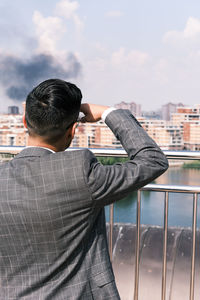 Rear view of man standing by railing in city against sky