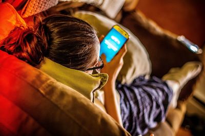 Mid adult woman using phone while lying on sofa at home