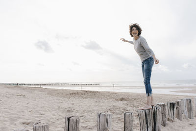 Happy woman balancing on wooden stake on the beach