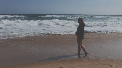 Rear view of woman standing on beach against sky