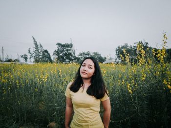 Portrait of young woman standing at rape farm against clear sky