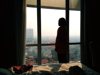 Silhouette woman looking through window at home