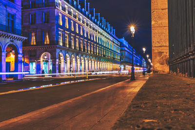 Illuminated light trails on street amidst buildings in city at night