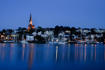 Illuminated buildings by river in city at dusk